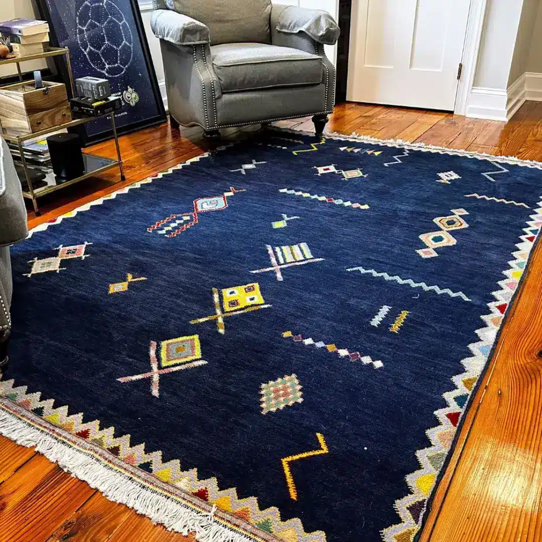 Handwoven deep navy Moroccan rug with colourful Berber geometric symbols on hardwood floor