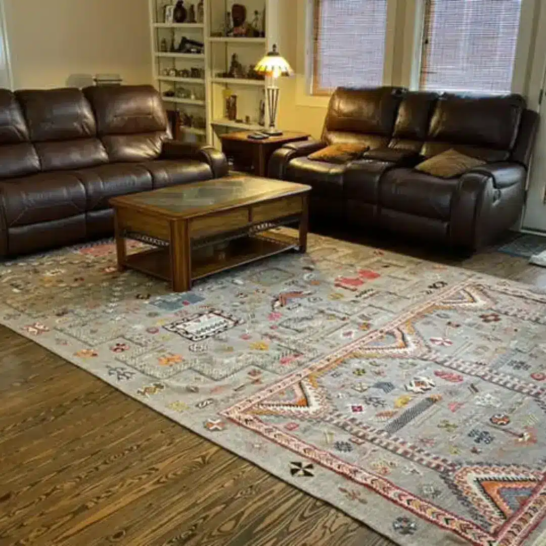 Large grey tribal Moroccan rug with terracotta and blush motifs under dark leather sofas on hardwood floor
