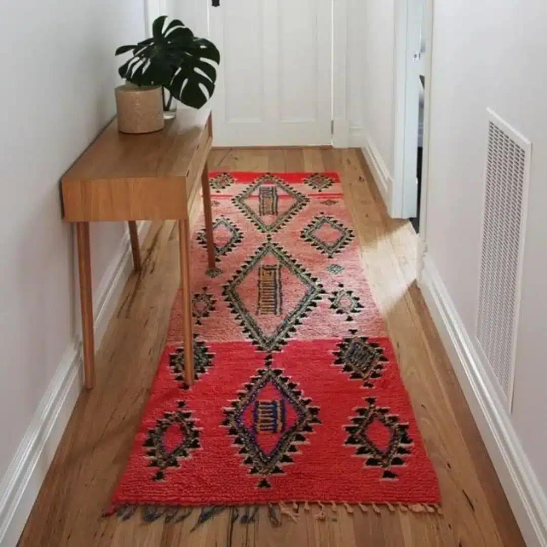 red Moroccan-style washable runner rug in a narrow hallway with wooden floor and console table